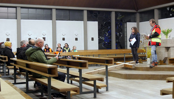 Die Kirche St. Alban in Erbshausen. Links sitzen Menschen mit dem Rücken zur Kamera. Rechts stehen zwei Personen und lesen etwas vor.