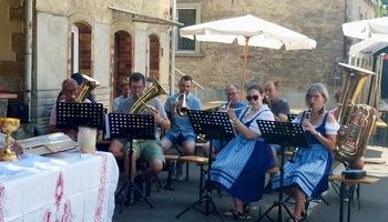 Das Bild zeigt eigen Blaskapelle aus 10 Personen. Die Frauen im Vordergrund haben blaue Dirndl an.